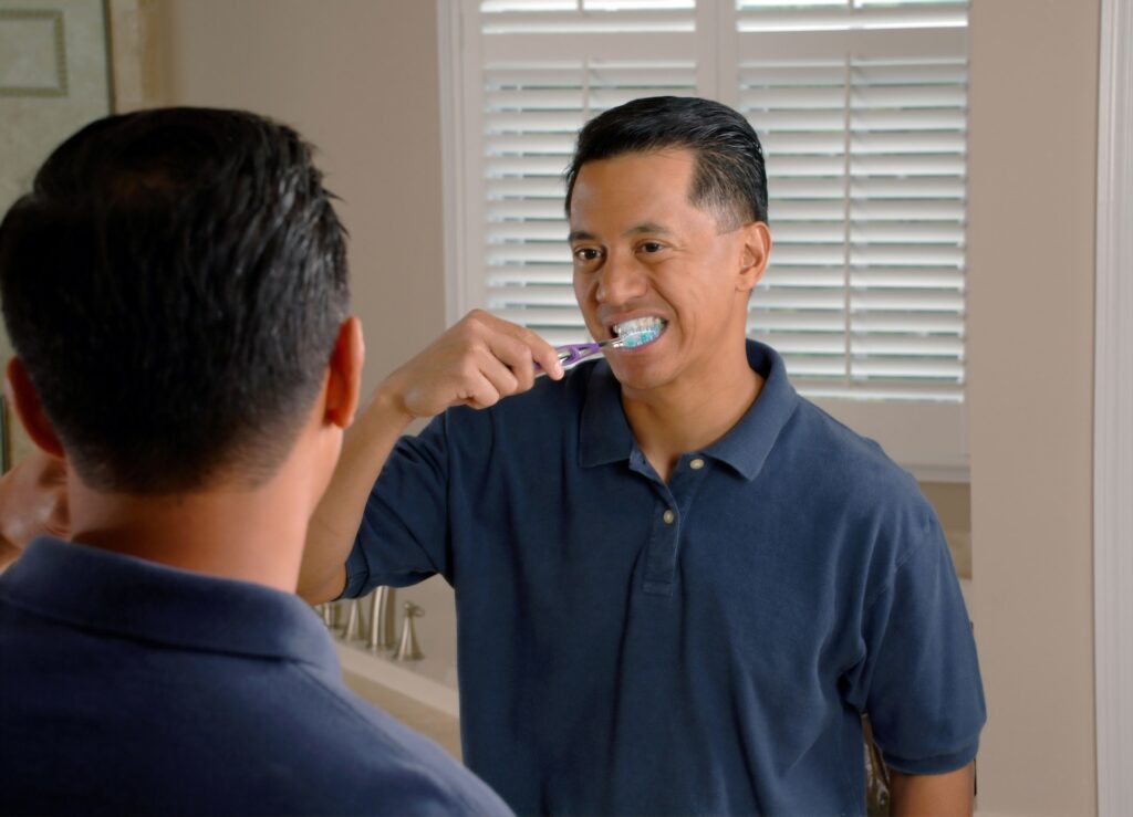 man brushing teeth while looking in mirror