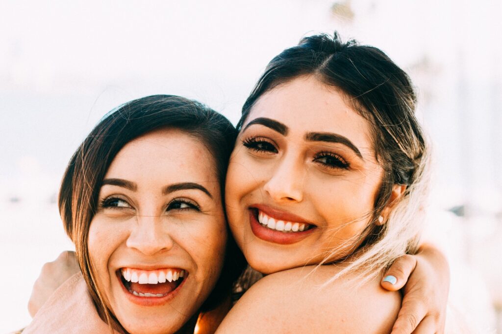 two women hugging and smiling with white background